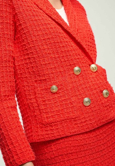 Červený texturovaný blazer s dvouřadým designem, velkými zlatými knoflíky a límečkem. Výrazné detaily kapes, vyrobený z tkané látky.