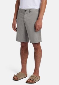 Pantaloni corti grigi chiari realizzati in misto cotone, con chiusura anteriore a bottone, tasche angolate e una vestibilità rilassata. Indossati con sandali beige.