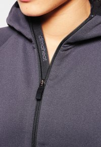 Felpa grigia con zip, dotata di un colletto alto e una zip nera prominente. Presenta il marchio "climaheat" lungo la linea della zip e una consistenza liscia.