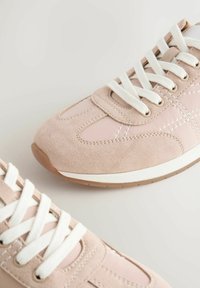 Baskets rose clair en daim et matériau synthétique, avec des lacets blancs, des détails de couture et une semelle en caoutchouc.