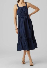 Marinblå, ärmlös klänning med fyrkantig halsringning, samlad midja och volangkant. Tillverkad av lätt tyg, med vertikala sömnadsdetaljer.