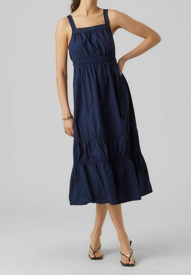Marinblå, ärmlös klänning med fyrkantig halsringning, samlad midja och volangkant. Tillverkad av lätt tyg, med vertikala sömnadsdetaljer.