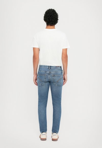 Jeans in denim azzurro chiaro con una vestibilità slim, design a cinque tasche e dettagli di cucitura sottili sulle tasche posteriori. Maglietta bianca indossata.
