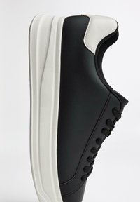 Schwarze Sneaker mit einer weißen Sohle, ausgestattet mit einem Obermaterial aus glattem Leder, runder Zehenpartie, Schnürdesign und strukturierten Akzenten an der Ferse.