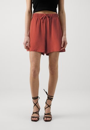 Rust-colored shorts with a textured fabric, elastic waistband, and drawstring. Paired with black strappy sandals, showcasing a casual look.