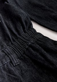 Gros plan d’un tissu en denim noir montrant une taille élastique froncée et des passants de ceinture sur un pantalon.