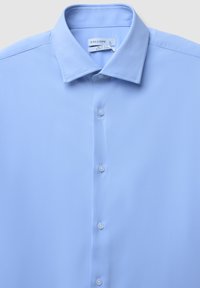 Helles Blau, schmal geschnittenes Hemd mit Knopfleiste und spitzem Kragen, Etikett in Größe L und pflegeleichtem Material.