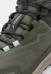 Close-up of an olive green Adidas Terrex hiking shoe with black and white dotted laces and light blue lace loops.