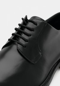 Scarpa da uomo nera in pelle con finitura lucida, dotata di sei fori per i lacci e una punta arrotondata liscia. Dettagli di cucitura lungo la suola.