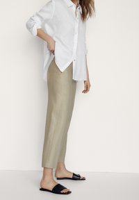 Camicia bianca in lino con bottoni, pantaloni su misura verde chiaro e sandali neri piatti. La camicia ha le maniche arrotolate e una vestibilità rilassata.