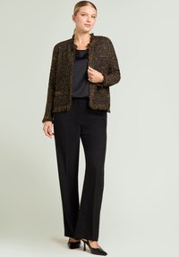 Black and gold textured jacket with frayed edges, paired with a black top and wide-leg pants, complemented by black heels.