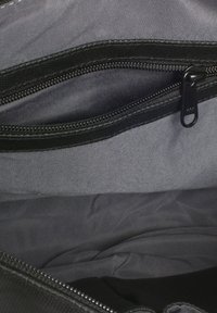Interno della borsa nera caratterizzato da un morbido tessuto grigio con una tasca con zip. La texture è liscia, con un design pulito e minimalista.