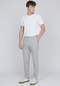 Pantaloni gri deschis, croiți pe măsură, cu o potrivire slim, asociați cu un tricou alb cu guler rotund și adidași albi cu accente verzi.