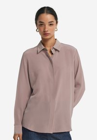 Jasnoróżowa bluzka z długim rękawem, z kołnierzykiem i zapięciem na guziki, wykonana z gładkiego, płynnego materiału. Charakteryzuje się luźnym krojem.
