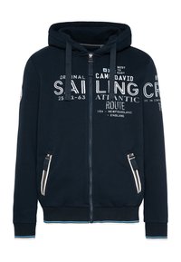 Felpa con zip colore navy realizzata in tessuto morbido. Presenta grafiche testuali bianche, tasche frontali con cerniere e orlo a coste con accenti blu.