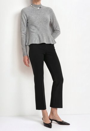 Woman wearing a grey ribbed sweater with flared hem, black straight-leg pants, black pointed-toe mules, and a silver necklace.