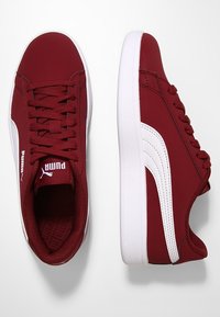 Zapatillas sintéticas rojas con acentos blancos, que cuentan con una puntera redondeada, diseño con cordones, collar acolchado y plantilla texturizada.