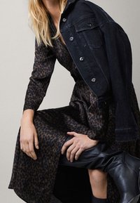Robe à imprimé léopard avec des manches longues, assortie à une veste en denim foncé ajustée. Texture lisse, bottes noires montant jusqu'aux genoux.