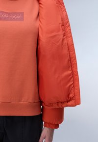Oranje hooded sweatshirt met een logo op de borst, met een dikke, geïsoleerde mouw die aan de pols gather. Glad van textuur.