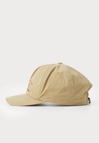 Beige bomull baseball cap med buet brem, brodert logo på fronten og justerbar stropp bak. Teksturerte stoffoverflaten.