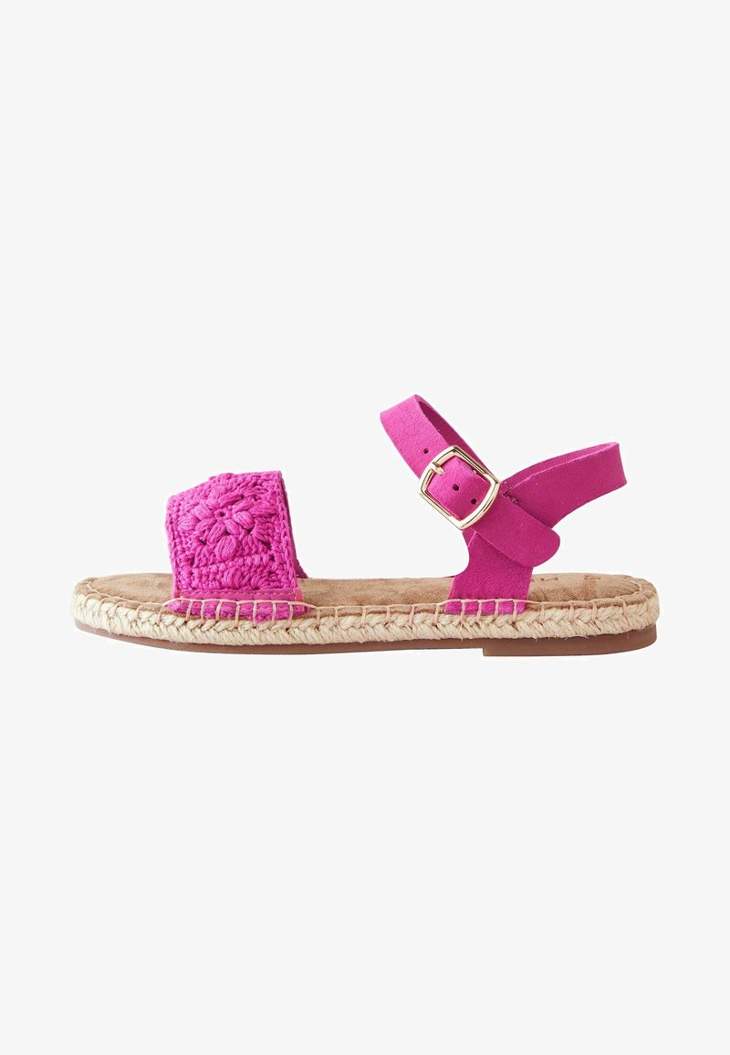 Sandales roses avec un design floral en crochet sur la lanière avant, une lanière de cheville en daim avec une boucle dorée, et une semelle en jute de style espadrille.