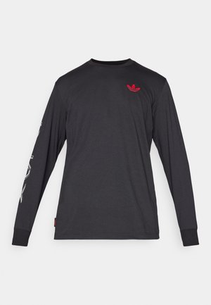 Camisa negra de manga larga hecha de suave algodón, con un pequeño logotipo rojo en el pecho y un detalle de texto en la manga izquierda.