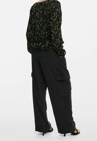 Blouse noire à imprimé floral avec manches à volants, portée avec un pantalon cargo noir ample doté de poches latérales et d'une texture lisse. Sandales à talons hauts.