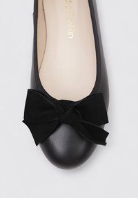Bailarinas negras de cuero suave, con punta redondeada y un gran lazo de terciopelo negro en la parte delantera. Logo dorado en relieve en el interior.