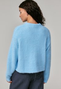 Suéter fofinho azul claro com decote redondo, design cropped e bainha canelada, combinado com calças listradas escuras.