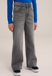 Helleblaue weite Jeans aus Denim mit hoher Taille, die gefärbte Taschen und eine glatte Textur aufweisen. Kombiniert mit schwarzen Sneakers aus Canvas.
