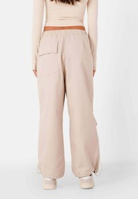 Lichtbeige wijde broek gemaakt van gladde stof, met een achterzak en verstelbare trekkoorden bij de enkels.