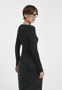 Czarna prążkowana bluzka z długim rękawem w połączeniu z skórzaną spódnicą do kolan. Bluzka ma dopasowany krój i okrągły dekolt.