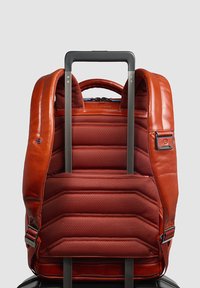 Mochila de cuero marrón con textura acolchada, equipada con correas ajustables, cierre de cremallera y asa retráctil para un transporte fácil.