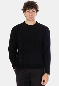 Maglione nero a girocollo realizzato in tessuto morbido e strutturato; presenta maniche lunghe e orlo a coste, indossato da una modella su sfondo chiaro.