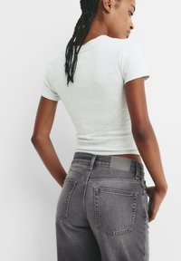 T-shirt slim fit grigio chiaro a maniche corte abbinato a jeans a vita alta grigio scuro con una patch in pelle e tasche posteriori.