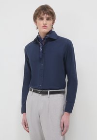 Camicia a maniche lunghe blu navy con bottoni, in misto cotone, con colletto a punta. Indossata con pantaloni grigi chiari su misura e una sciarpa blu navy.