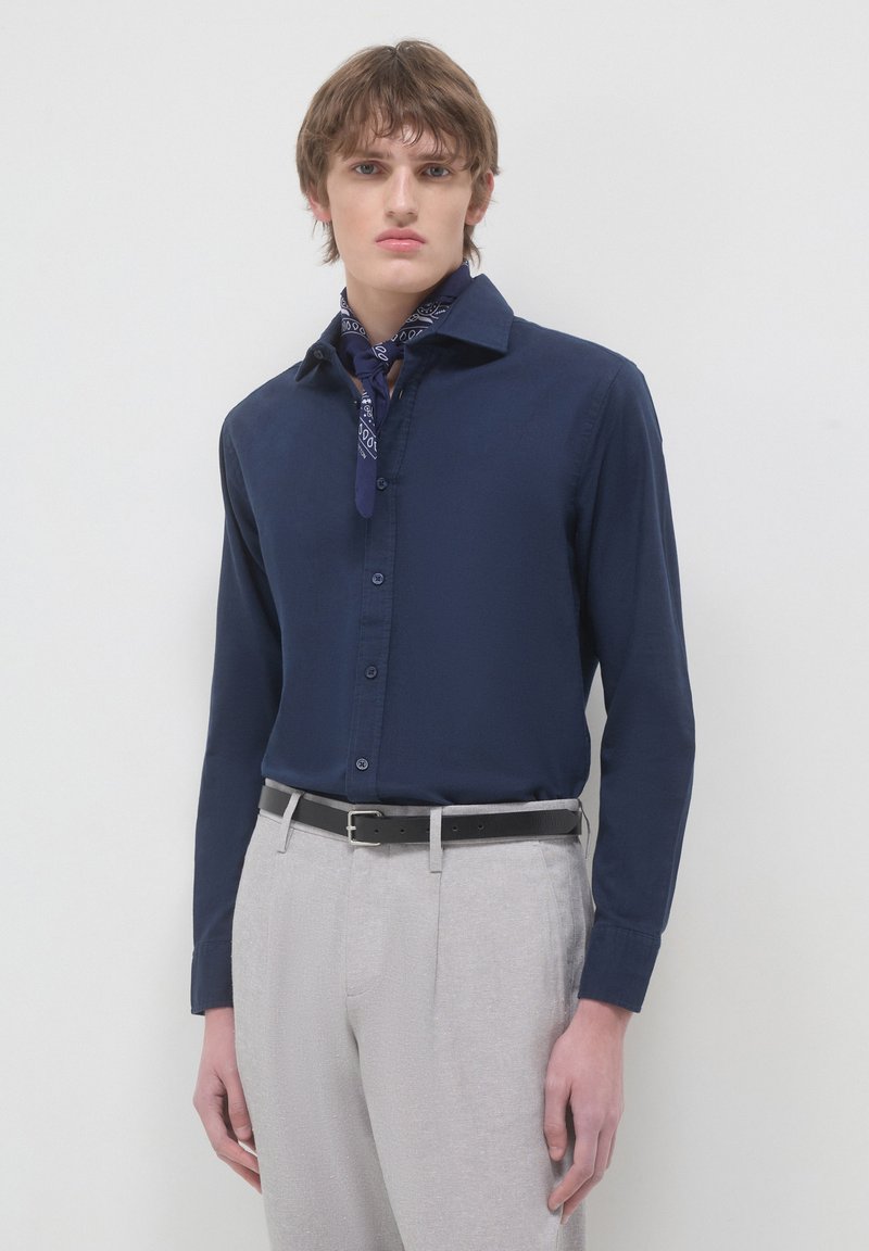 Camicia a maniche lunghe blu navy con bottoni, in misto cotone, con colletto a punta. Indossata con pantaloni grigi chiari su misura e una sciarpa blu navy.