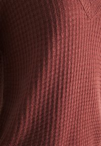 Maglione lavorato a maglia bordeaux con scollatura a V, caratterizzato da un motivo a coste texturizzato e una finitura morbida, che mette in evidenza il suo aspetto caldo e accogliente.
