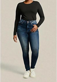 Top negro de manga larga combinado con jeans ajustados de cintura alta en azul oscuro. Los jeans presentan un ligero desgaste y se completan con zapatillas blancas.