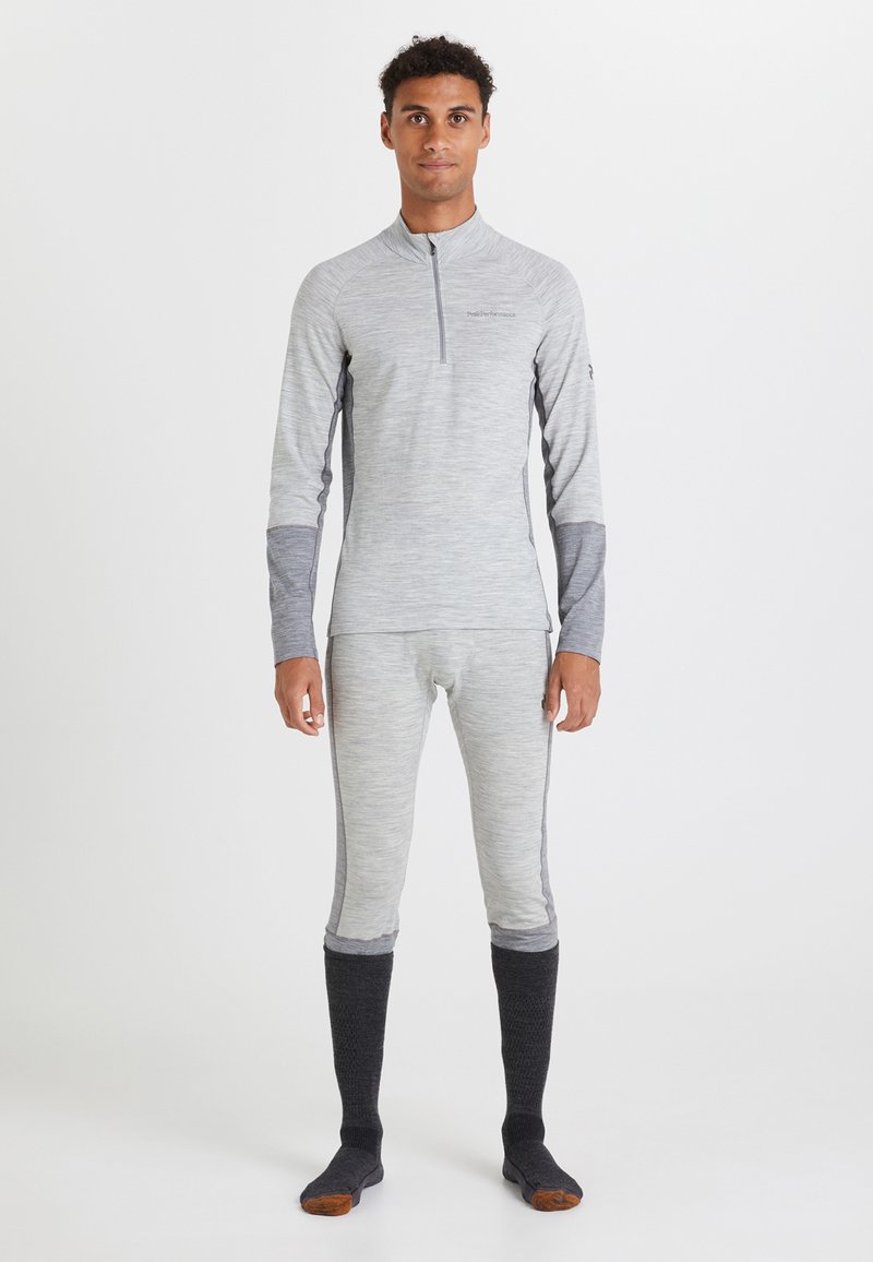 Maglietta termica grigia da performance con mezza zip, maniche lunghe e dettagli grigi testurizzati in contrasto. Abbinata a leggings grigi coordinati e calzini scuri.