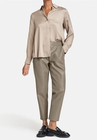 Beige satin skjorta med knappar, lös passform och långa ärmar, tillsammans med olivgröna imitationläderbyxor som är smalare nere och svarta loafers.