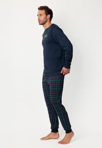 Sudadera azul marino con el texto "EXTREME" en multicolor; pantalones de pijama a cuadros en azul marino, verde y rojo. Puños ajustados, tela suave, diseño casual.