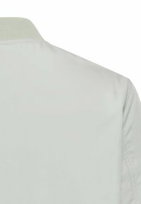 Lys grå bomberjakke med tekstureret krave, glat stof og minimalistisk design uden synlige hardwaredetaljer eller accenter.