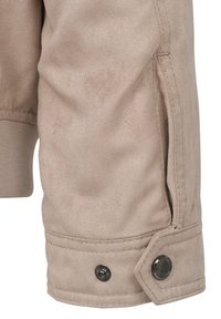 Beige outerwear featuring a smooth texture, elastic cuff, and snap button detail on the sleeve hem. Includes a side zip pocket.