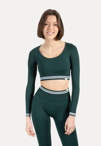Zielony sportowy krótki top z długimi rękawami, z białym paskiem w paski na talii. Do kompletu legginsy z wysokim stanem, które dopełniają zestaw.