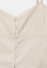 Haut sans manches couleur crème avec fines rayures verticales sur la partie supérieure, bordure en dentelle le long de la couture et boutons au centre devant.
