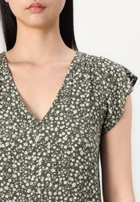 Grünes Blumenkleid mit V-Ausschnitt, kurzen Schmetterlingsärmeln und einem leichten Stoff mit kleinen weißen Blumen und einem zarten Muster.