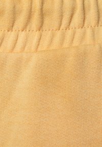 Helles gelbes Gewebe mit einem glatten, texturierten Strick, das einen gerafften elastischen Bund und feine Nähte an den Rändern aufweist.