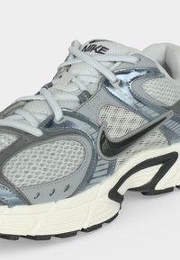 Λευκό και γκρι παπούτσι τρεξίματος Nike με μαύρο λογότυπο Swoosh, τμήματα από διχτύ, λευκά κορδόνια και παχύ μαλακό πέλμα.