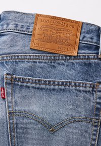 Blå denimjeans bakficka med orange sömmar, en röd Levi's-tag och en brun läderetikett från Levi Strauss & Co. som visar storlek W32 L32.
